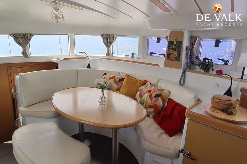 Een interieur van een boot met een witte U-vormige bank, een ovale houten tafel en ramen met uitzicht op water.
