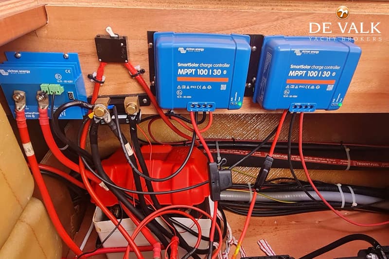 Drie blauwe Victron Energy SmartSolar laadregelaars zijn gemonteerd op een houten wand, omringd door rode en zwarte kabels.