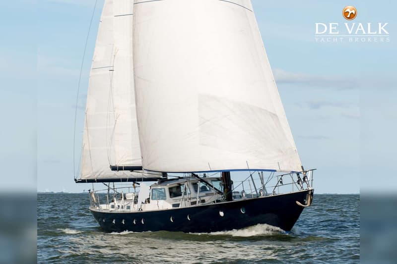 Een donkerblauwe zeilboot met witte zeilen vaart op het water onder een lichtblauwe lucht. — Robert Clark 64 Pilothouse