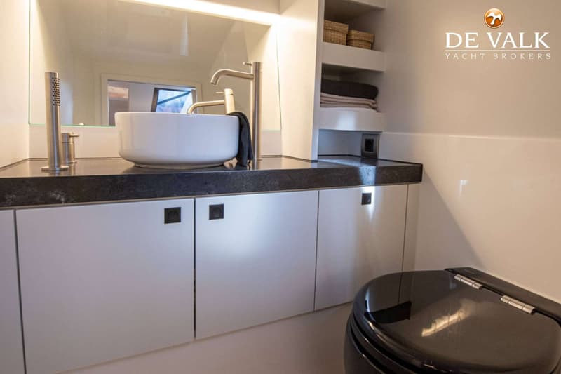 Een badkamer met een witte waskom, een zwarte wastafel en een zwart toilet, met daarboven een spiegel en planken.