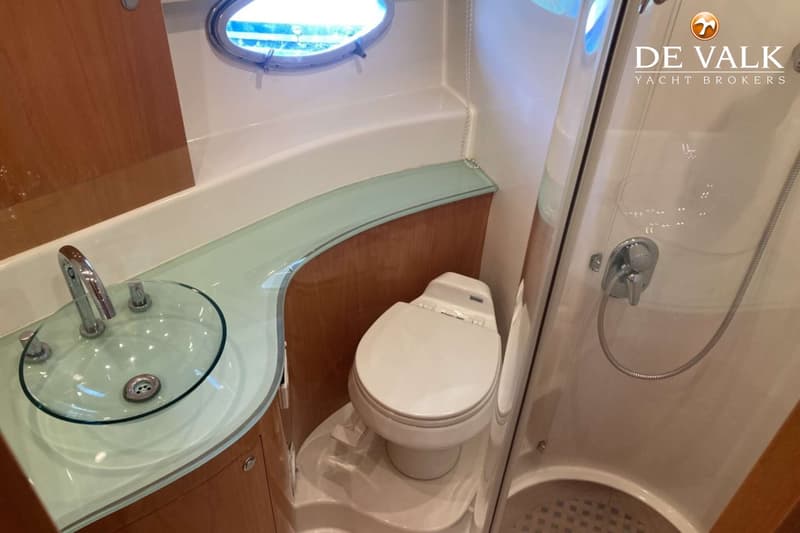Een badkamer met een glazen wastafel, een toilet en een douchecabine met een patrijspoort erboven.