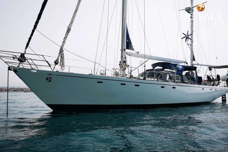 Een witte zeilboot met een blauwe kap en een windgenerator op de mast ligt in het water. — Picchiotti Laurent Giles 65
