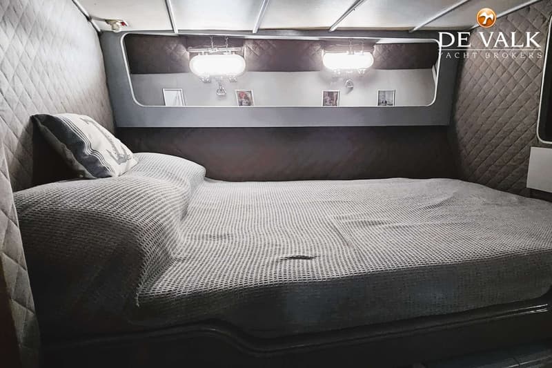 Een kajuit met een bed, een kussen met een anker erop, twee lampen en een spiegel met daarin foto's.