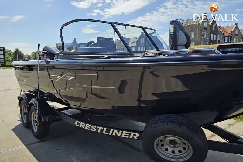 Een zwarte boot met een voorruit staat op een zwarte trailer met twee assen, onder een blauwe lucht.