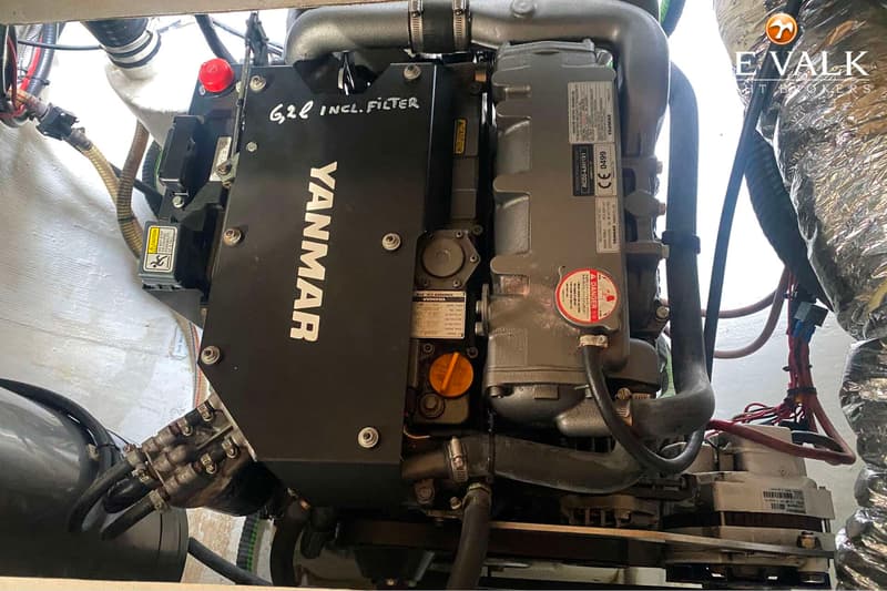 Een close-up toont een Yanmar scheepsmotor met diverse slangen, kabels en een waarschuwingssticker.