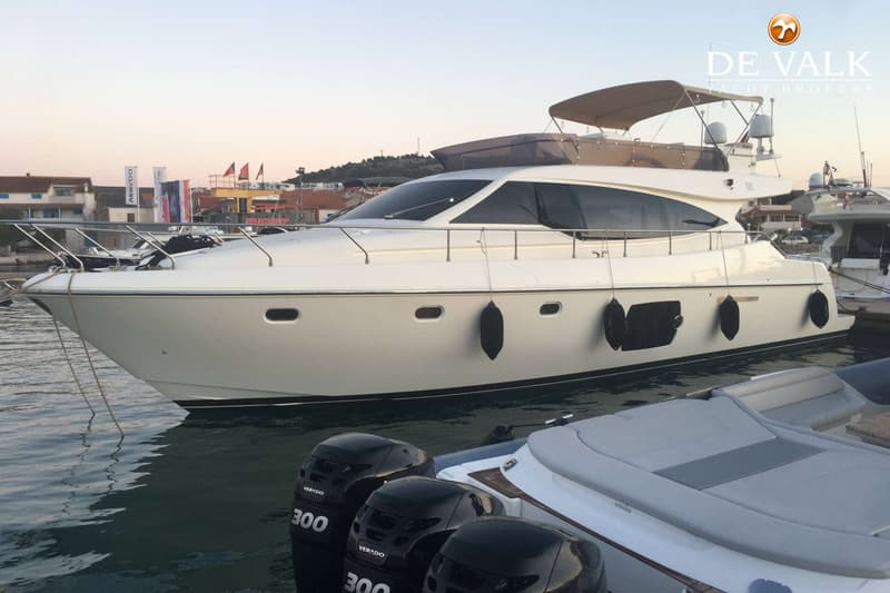 Een witte motorjacht met een bruine bimini-top ligt afgemeerd in een haven, met een kleinere boot ernaast. — Ferretti 510