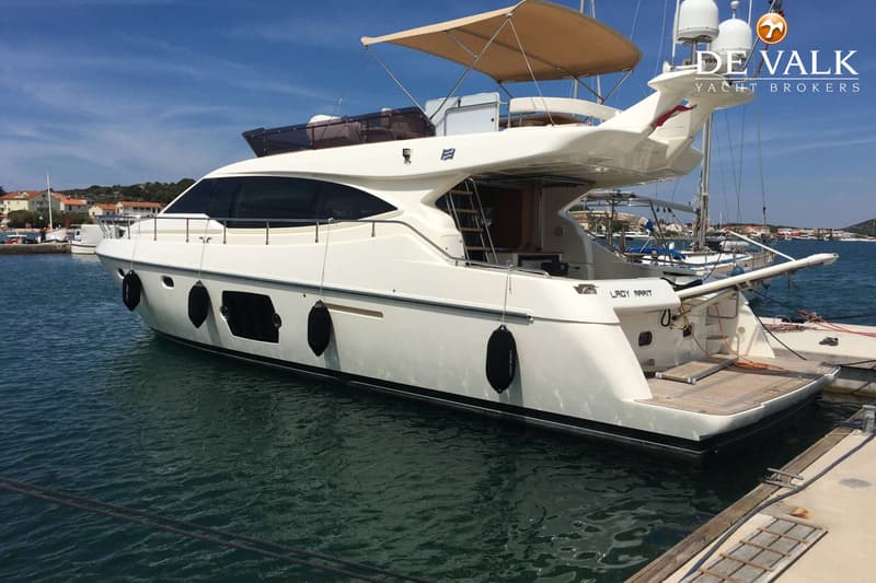 Een witte motorjacht met de naam "LADY MARIT" ligt aangemeerd in een haven, met een beige zonnescherm en zwarte stootwillen.