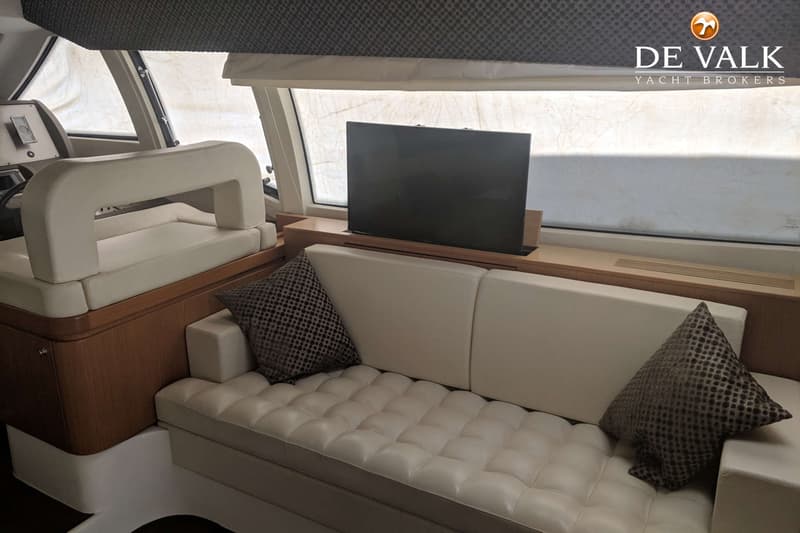 Een interieur van een boot met een beige bank, twee kussens, een televisie en een stuurstand. — Ferretti 510