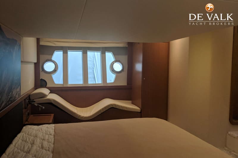 Een kajuit met een bed, een golvende bank, patrijspoorten en ramen, en een houten kast. — Ferretti 510