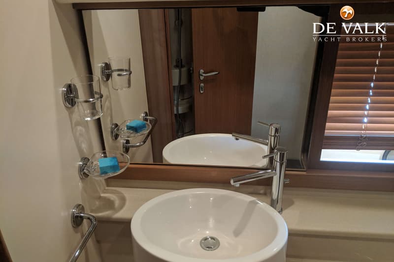 Een badkamer met een witte wastafel, een spiegel, twee zeepbakjes met blauwe zeep en een houten deur.