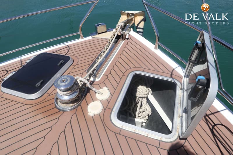 De foto toont de boeg van een boot met een ankerlier, ankerketting, touwen en twee luiken op een bruin dek. — Pilot 50