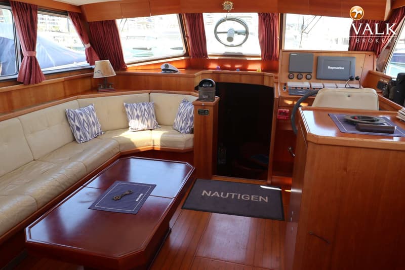 Een interieur van een boot met een beige bank, houten tafel, stuurwiel en navigatieapparatuur. — Pilot 50