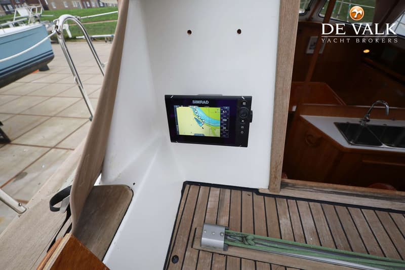 Een Simrad plotter met een kaartweergave is gemonteerd op een witte wand, met een houten vloer en een kajuitingang.