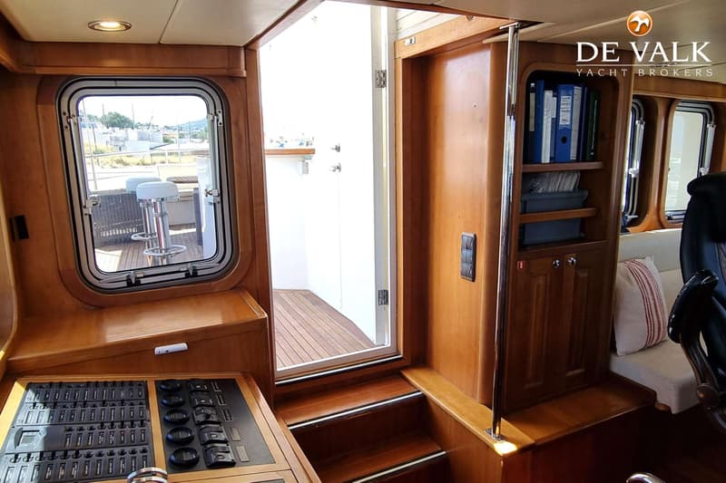 De foto toont het interieur van een boot met houten afwerking, een bedieningspaneel en een open deur naar het dek.