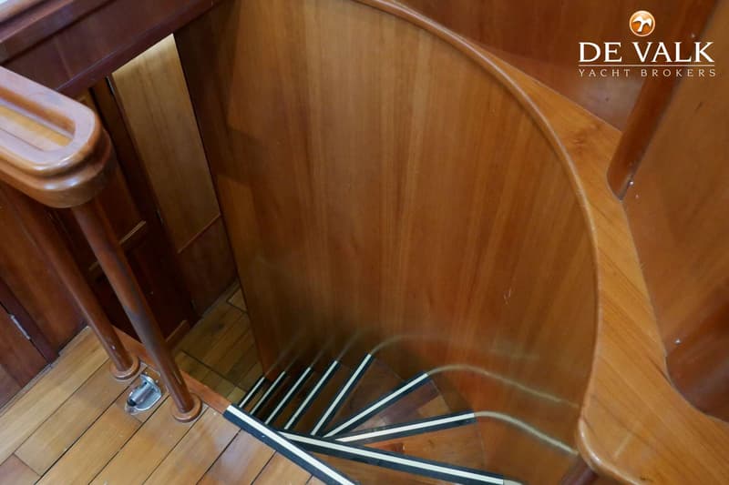 Een houten trap met witte en zwarte antislipstrips op de treden, een houten leuning en houten wanden.