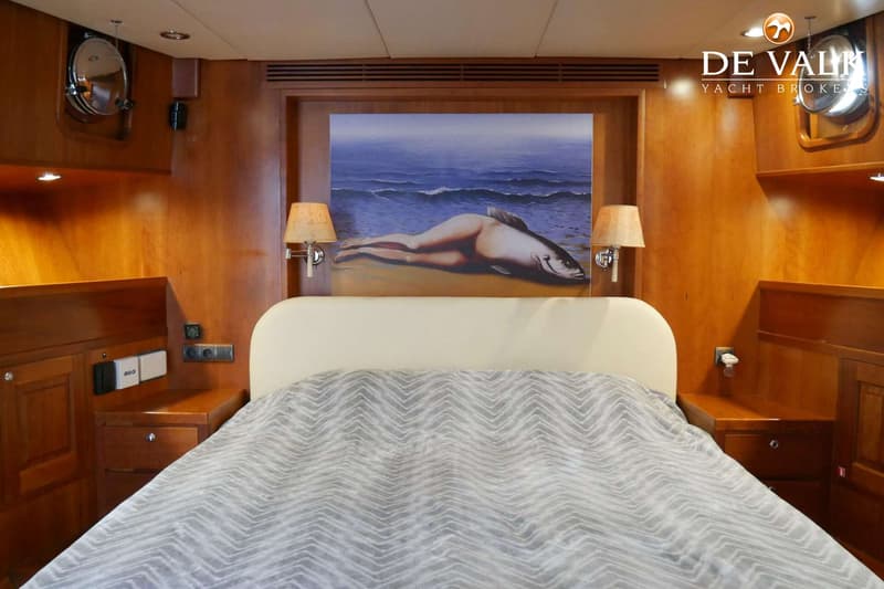 Een kajuit met een tweepersoonsbed, nachtkastjes, lampen, patrijspoorten en een schilderij boven het bed.