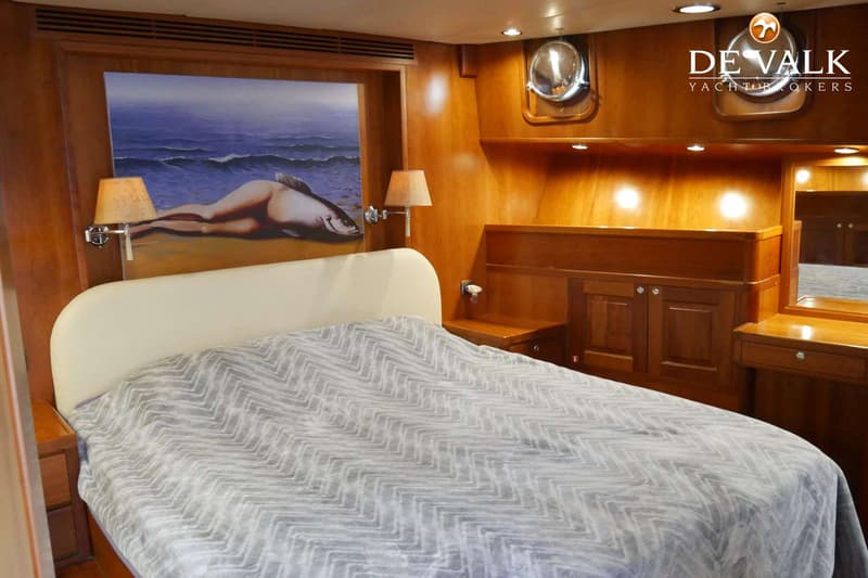 Een slaapkamer met een tweepersoonsbed, houten wanden, een schilderij, twee lampen en een patrijspoort.