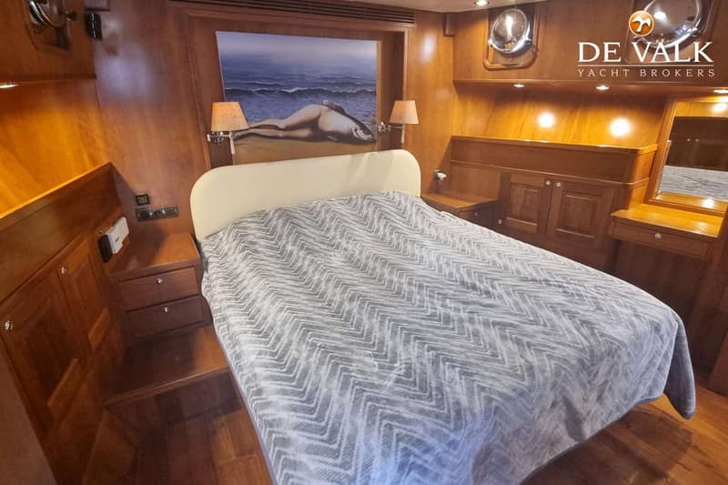 Een slaapkamer met een tweepersoonsbed, nachtkastjes, een schilderij boven het bed en houten wanden.