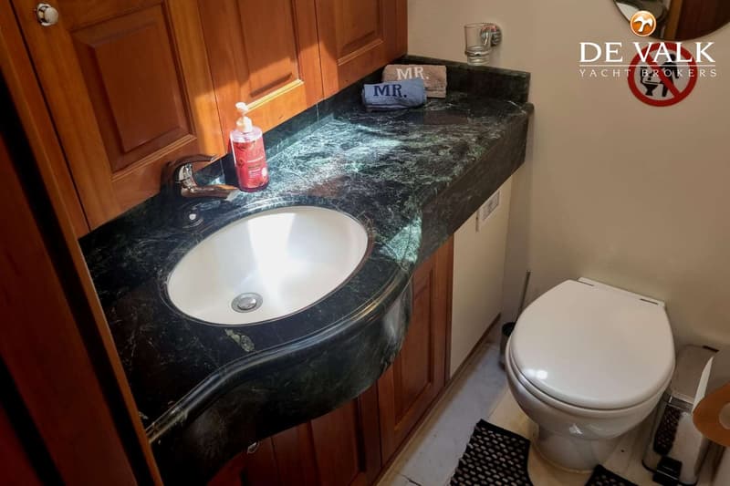 Een badkamer met een wit toilet, een wastafel met een donkergroen marmeren blad en houten kasten.