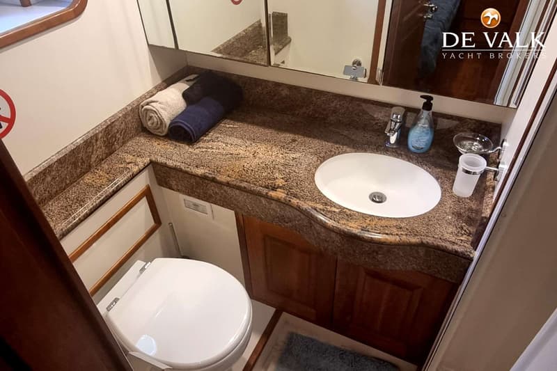 Een badkamer met een wit toilet, een wastafel in een granieten aanrechtblad en een spiegelkast erboven.