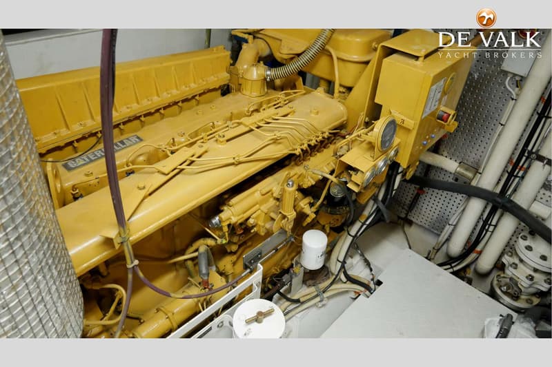 Een gele Caterpillar scheepsmotor met diverse leidingen en filters is zichtbaar in een motorruimte.