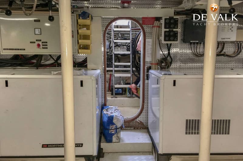 Twee witte generatoren flankeren een doorgang met een ladder, met diverse bedrading en panelen aan de wanden.