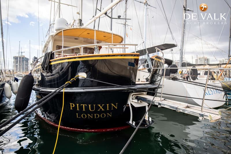 Een zwarte boot met de naam "PITUXIN LONDON" in gouden letters ligt afgemeerd in een haven.