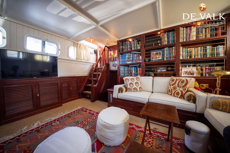 Een interieur van een boot met een witte bank, een boekenkast, een televisie en een trap.
