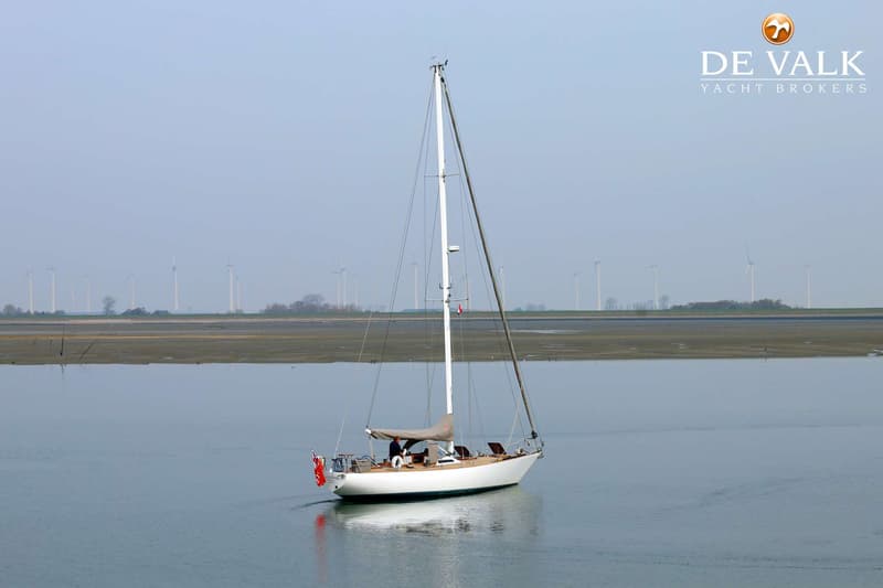Een witte zeilboot met een grijze huik ligt in rustig water, met windmolens op de achtergrond. — Dick Zaal 41