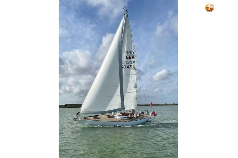 Een witte zeilboot met houten dek vaart op water onder een bewolkte hemel. — Dick Zaal 41