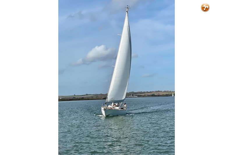 Een witte zeilboot vaart op het water met een landschap op de achtergrond onder een deels bewolkte hemel. — Dick Zaal 41