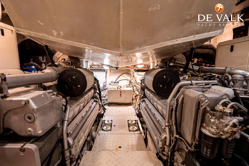 De foto toont een machinekamer met twee grote motoren aan weerszijden van een gangpad met een geribbelde metalen vloer.