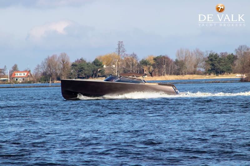 Een donkerbruine motorboot vaart over blauw water, met een huis en bomen op de achtergrond. — VanDutch 40