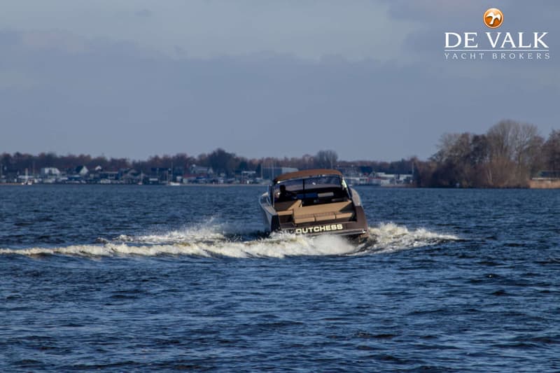 Een motorboot met de naam "DUTCHESS" vaart op het water, met een dorp en bomen op de achtergrond. — VanDutch 40