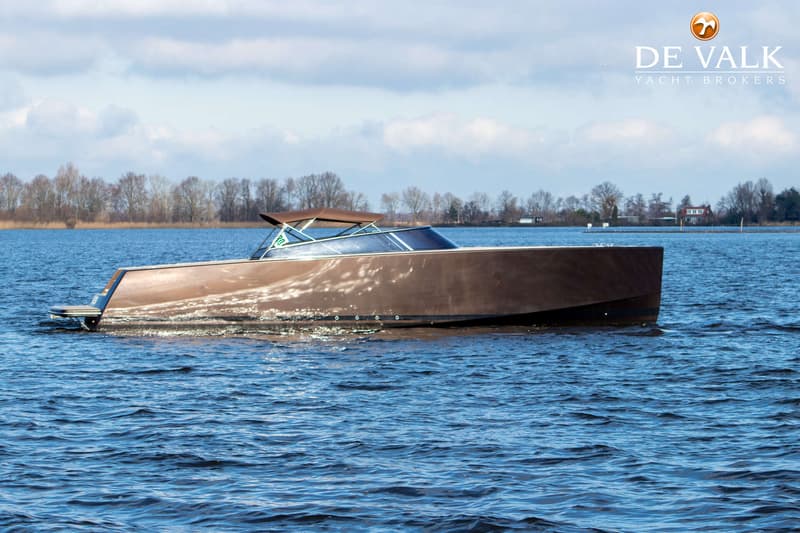 Een bruine motorboot vaart op een waterweg met een beboste oever op de achtergrond onder een bewolkte hemel. — VanDutch 40