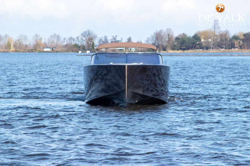 Een donkere boot met een bruine kap vaart op het water, met een beboste oever op de achtergrond. — VanDutch 40