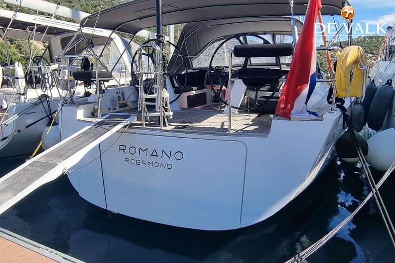 De achterkant van een witte zeilboot met de naam "ROMANO ROERMOND" is zichtbaar, met een loopplank en een Nederlandse vlag.