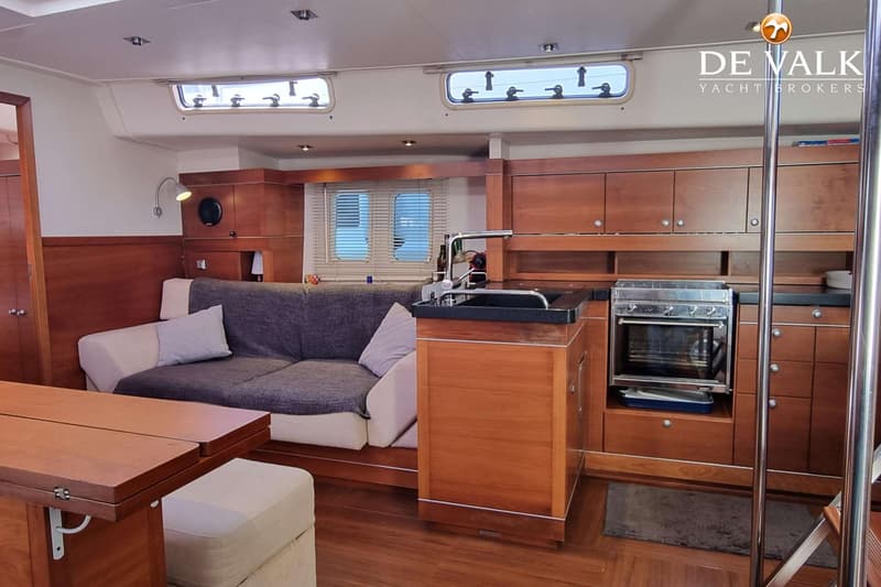 Een interieur van een boot met een zithoek, een kombuis met gootsteen en fornuis, en houten kasten. — Hanse 545