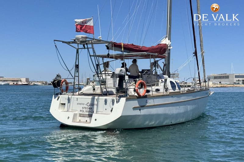 Een witte zeilboot met een Poolse vlag vaart op helderblauw water, met twee personen aan boord. — Custom Built Audax 47