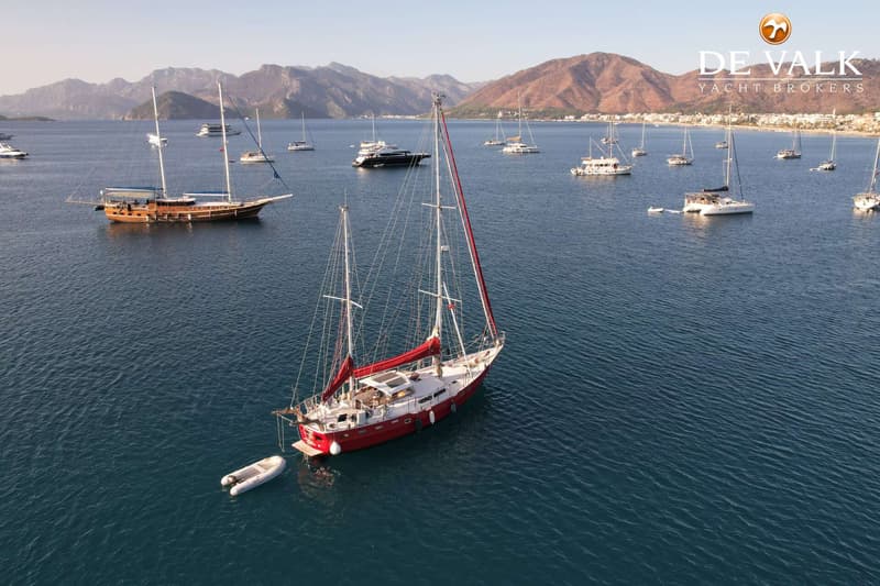 Een rode zeilboot met een bijboot ligt voor anker in een baai met bergen op de achtergrond. — Suncoast 48