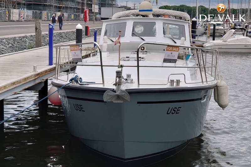 Een grijze boot met de naam "USE" op de boeg ligt aangemeerd aan een houten steiger. — Pilot 44