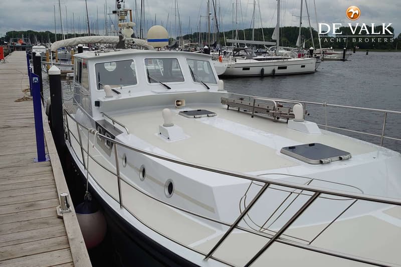 Een witte motorboot ligt afgemeerd aan een houten steiger, met andere boten op de achtergrond. — Pilot 44