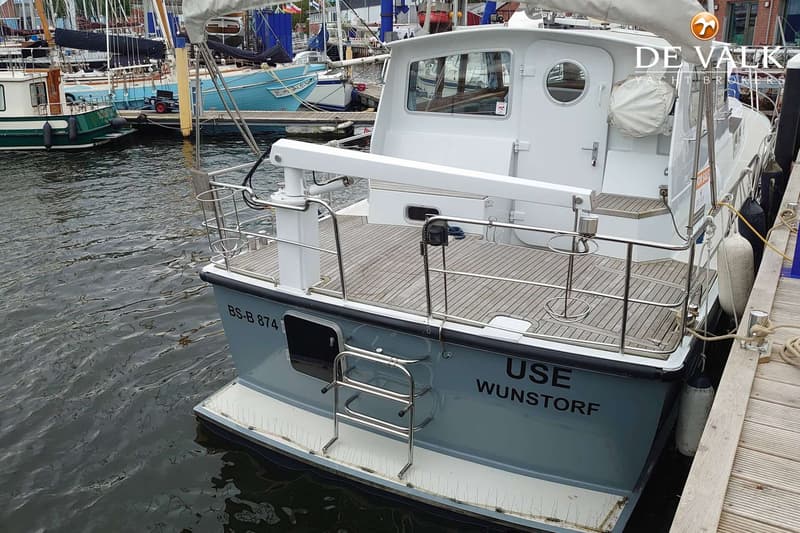 Een grijze boot met een wit dek en een houten vloer ligt aangemeerd, met de tekst "USE WUNSTORF" en "BS-B 874" op de romp.