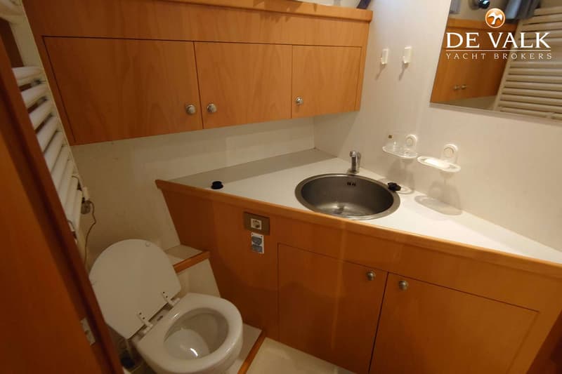 Een toiletruimte met een wit toilet, een ronde metalen wasbak met kraan, en houten kasten en panelen.