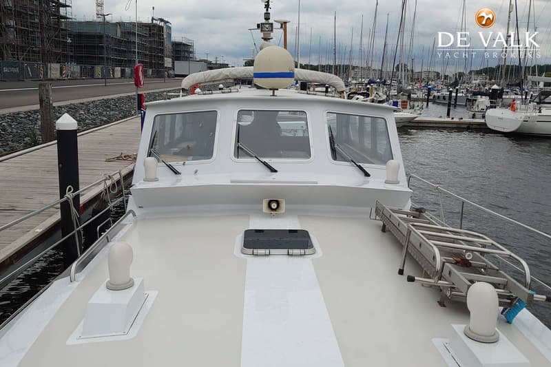 Een witte boot met een stuurhut, patrijspoorten, een luik en een ladder op het voordek, aangemeerd aan een steiger.