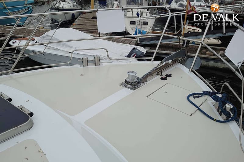 De boeg van een boot met een ankerlier, ankerketting, bolders en een blauwe lijn, met een bijboot en andere boten op de…