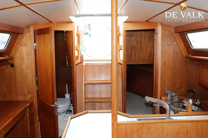 De foto toont het interieur van een boot met houten wanden, een wit plafond, een toiletruimte en een kombuis met spoelbak.