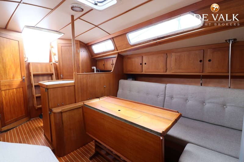 De foto toont het interieur van een boot met houten lambrisering, een opklapbare tafel en grijze zitbanken. — Faurby 396