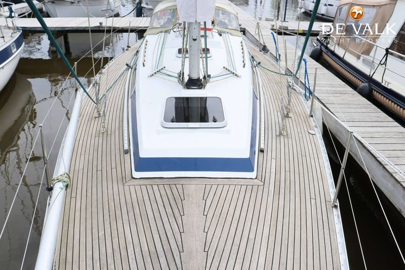Een bovenaanzicht van het dek van een zeilboot met een houten dek, witte opbouw en blauwe streep. — Faurby 396