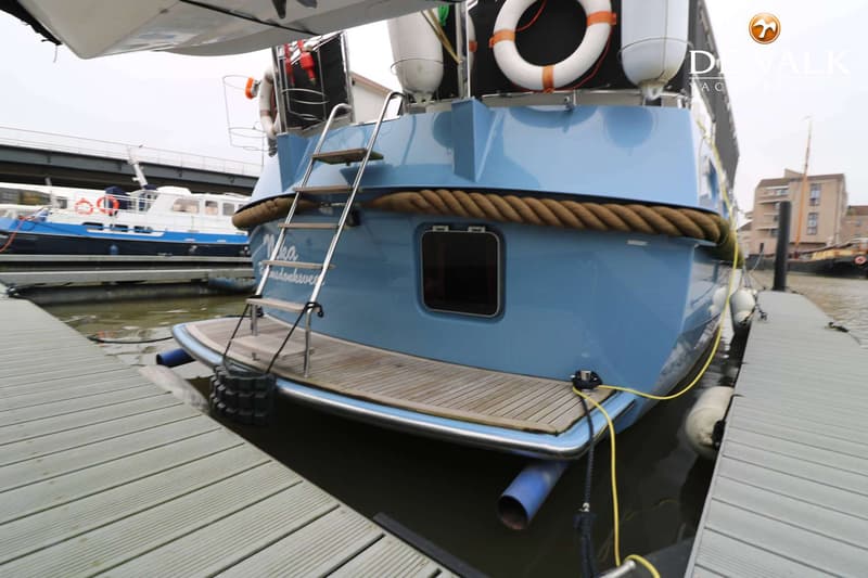 De achterkant van een lichtblauwe boot met een zwemplateau en een trapje, afgemeerd aan een steiger.
